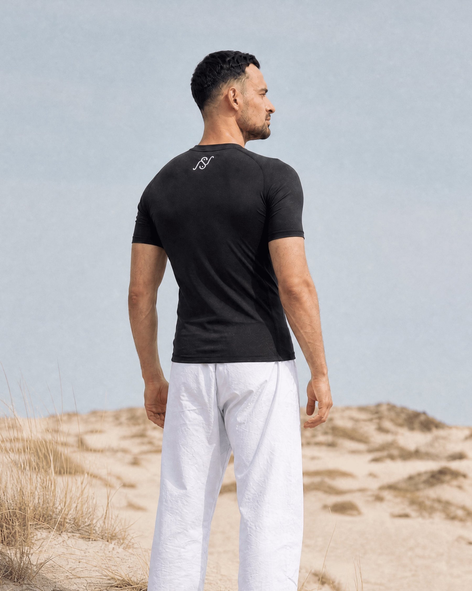 Back view of a man in the black V1 Hybrid compression shirt, white NS monogram at the neck